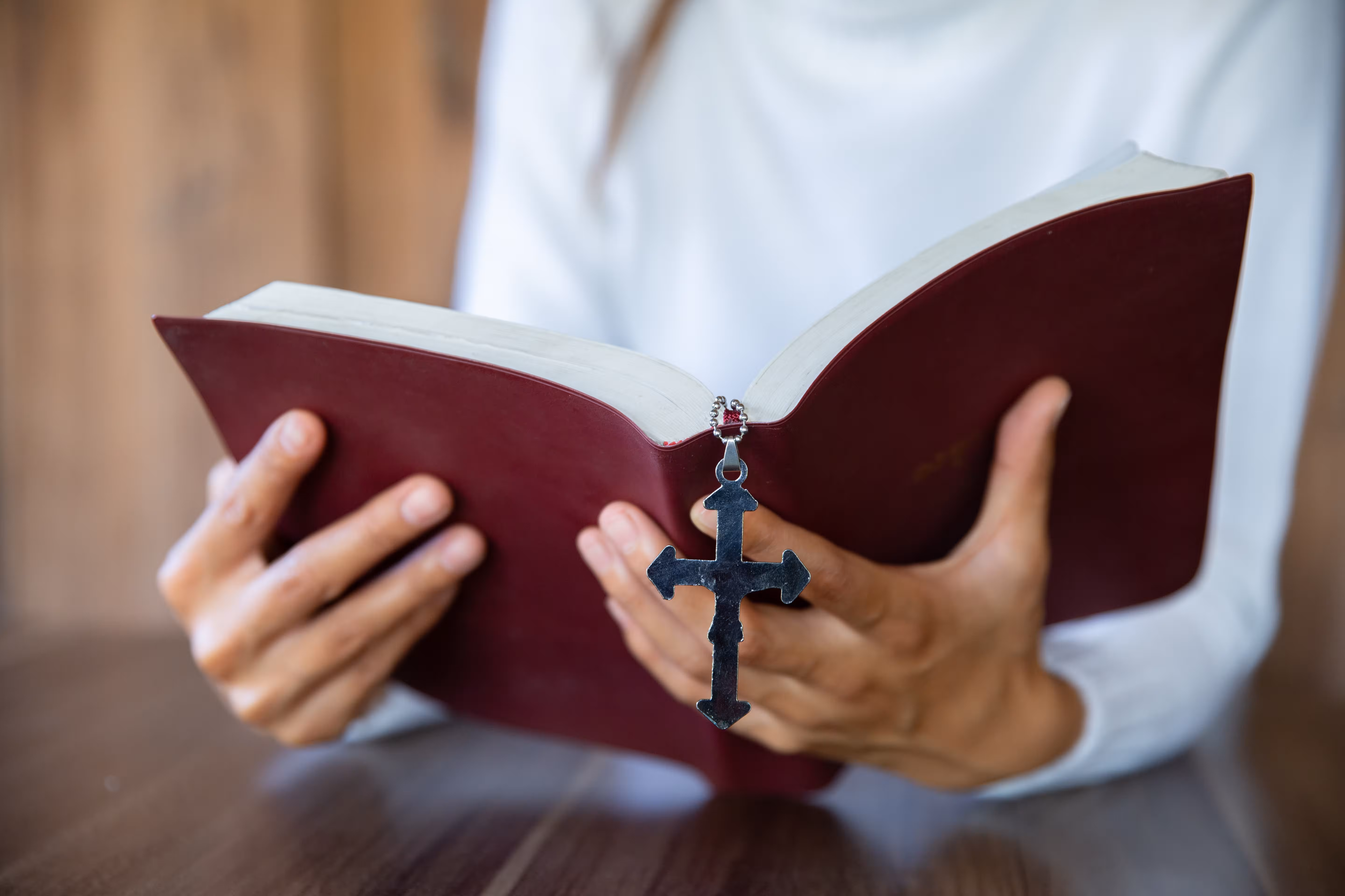 Person hält eine offene burgunderrote Bibel mit einem sichtbaren Kreuz-Lesezeichen zwischen den Seiten
